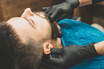 Haircut head and beard in a barbershop. Barber puts on and combs client&rsquo;s beard. Process of creating a hairstyle and styling a beard for men. Man in a barbershop. Equipment stylist. Selective focus