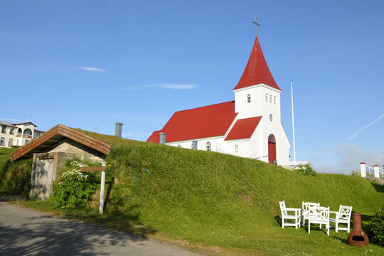 Die schöne Dorfkirche von Kirche von Hrisey, Island mit einem Gebäude mit Grasdach im Vordergrund