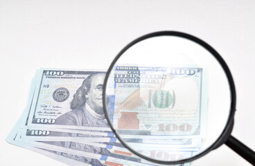 Magnifying glass and dollars on a white background. 100 dollars banknote view through a magnifying glass