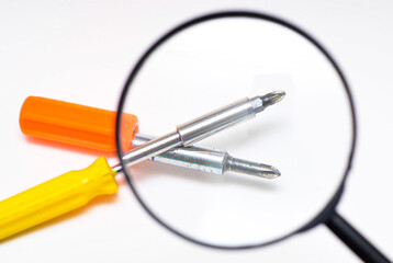 Magnifying glass and Phillips screwdrivers with a yellow and orange pen on a white background. View of tools screwdriver through a magnifying glass
