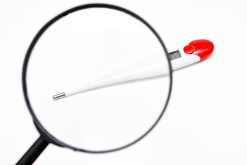 Magnifying glass and medical electronic thermometer, thermometer on a white background. View of a medical thermometer through a magnifying glass