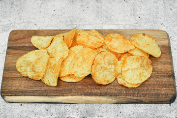 Corrugated potato chips on a wooden board. Snack, ready meal menu, junk food. Close up.