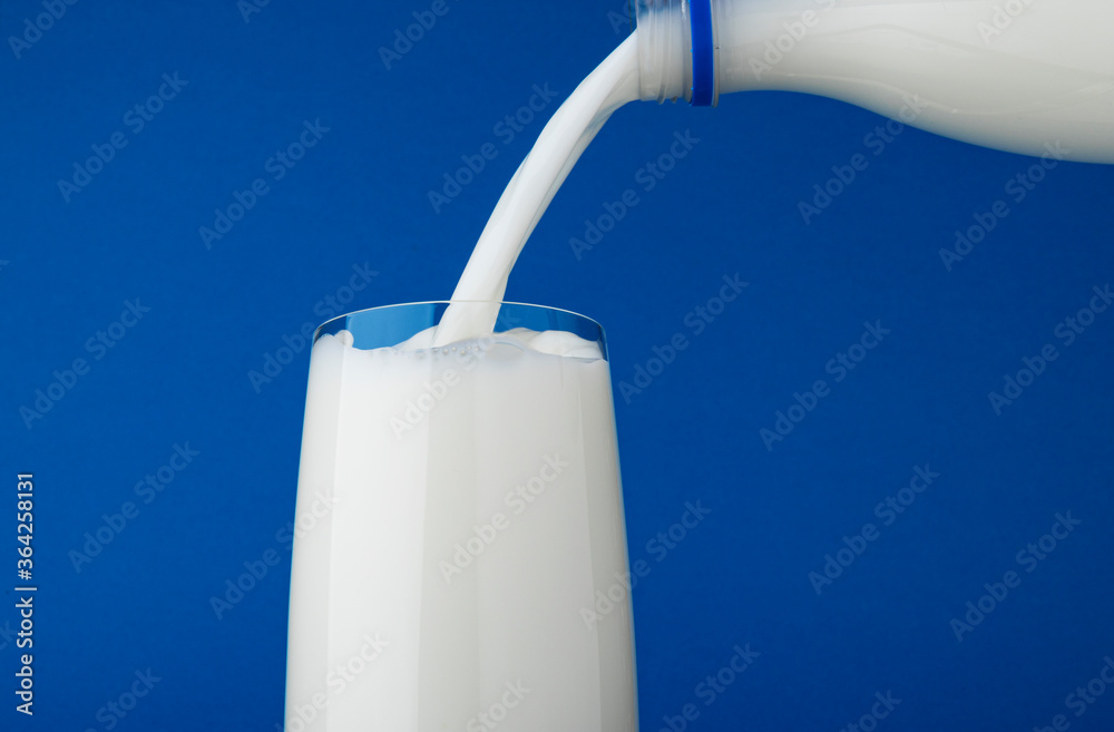 Wall mural pouring milk in glass isolated on blue background