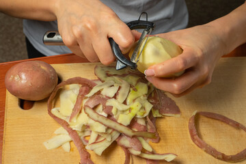 peeling potatoes with a knife for peeling vegetables. female hands peel potatoes over a wooden kitchen board while cooking