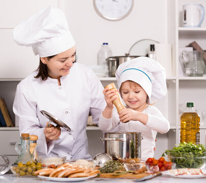 Girl and her mother are cooking soup together and adding spices in the kitchen at home.
