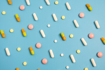 Close up of many different pills arranged in pattern on blue background.