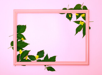 Red wooden picture frame decorated with small yellow flowers and green leaves on pink copy space background.