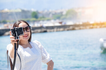 Asian beautiful woman is travel for holiday in the summer of Europe and taking a camera view landscape of lake and bright sky in Geneva Switzerland, copy space.