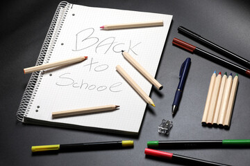 White notebook , color pencils, felt pen and pencil sharpener on a table against black background. Preparing for a school. Back to school.