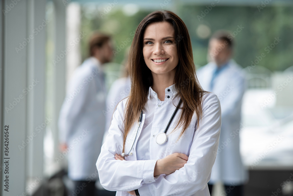 Wall mural portrait of young woman doctor with white coat standing in hospital.