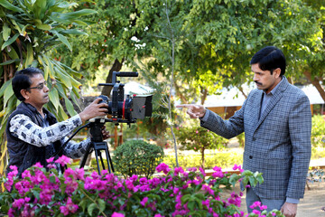 Professional Indian journalist and cameraman recording video interview. Cameraman in stylish jacket recording videos with professional camera and equipment.Shooting an interview in the park.