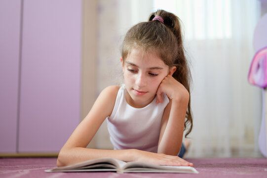 The girl lies on the floor and reads a book enthusiastically