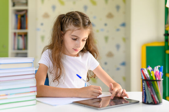 The girl does homework and uses the tablet. Girl schoolgirl sitting at a desk at home