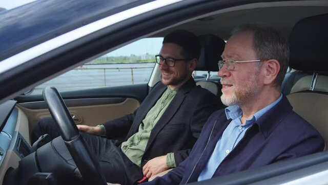 Two cheerful multi-age business colleagues discussing funny news and smiling on drive by modern car. Roadtrip. Business people. Father and son. Communication.