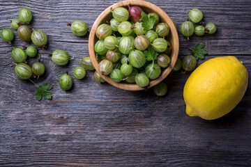 Fresh gooseberries in wooden bowl on wooden rustic background, top view.