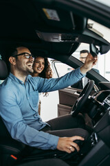 Middle age couple choosing and buying car at car showroom. Car salesman helps them to make right...