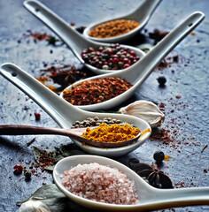 food photography of colored oriental (asian) spices in white spoons side view on a dark blue stone background in back light close up, macro