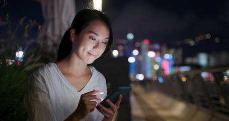Woman checks on mobile phone in city at night