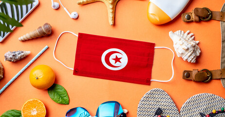 Fototapeta na wymiar Accessories for beach holidays around a protective mask with the flag of Tunis. Concept of leisure at sea during a pandemic. Top view