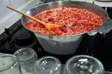 Cooking strawberry jam in a large bowl at home. Wooden spoon in a bowl with jam. Empty glass jars for jam.