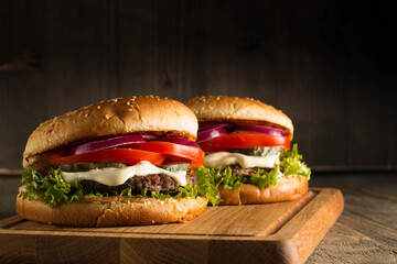 Home made hamburger with beef, onion, tomato, lettuce and cheese. Fresh burger close up on wooden rustic table with potato fries, beer and chips. Cheeseburger.