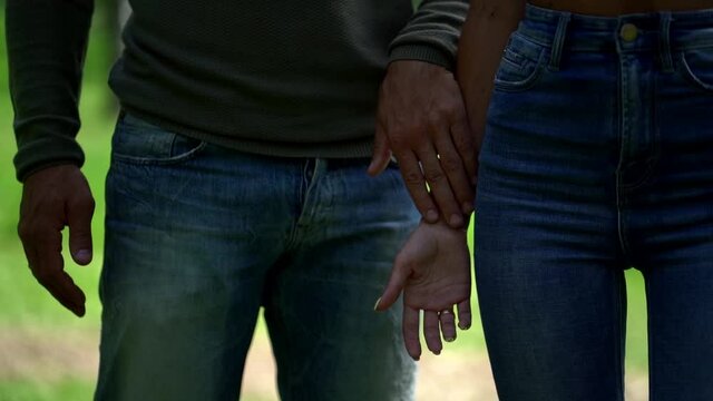a loving harmonious couple: a bald middle-aged man and a young slender girl in a top and jeans with a high waist, they walk through a summer Park, take each other's hands and look at each other.