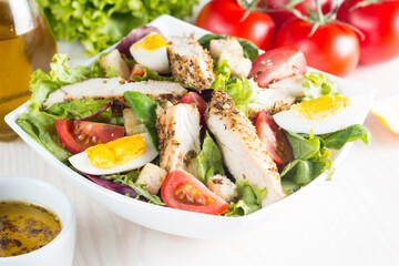 Fresh Caesar salad with delicious chicken breast, ruccola, spinach, cabbage, arugula, egg, parmesan and cherry tomato on wooden background. Oil, salt and pepper. Healthy and diet food concept.