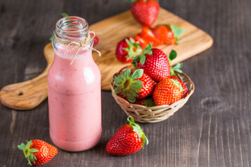 Glass of fresh strawberry milkshake, smoothie and fresh strawberries on pink, white and wooden background. Healthy food and drink concept.