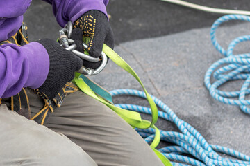 Worker fixes a rope and climbing equipment before descending from the roof. High-altitude works.