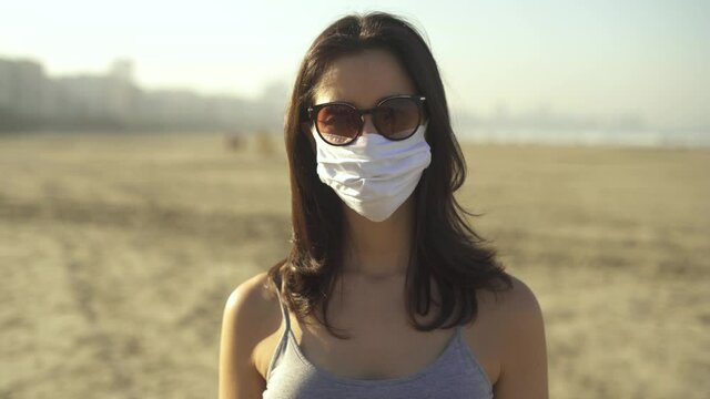 woman wearing face mask and sun glasses for corona virus prevention on the beach. Loosen restriction, reopen
