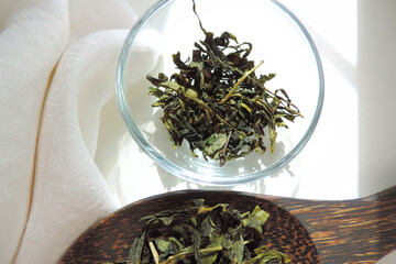    dry green tea leaves in a glass bowl      