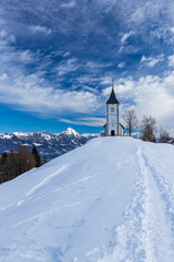 Fototapeta na wymiar Church of Saint Primus and Felician Jamnik Slovenia winter snow mountain Storžič