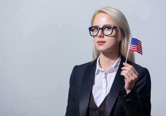 Beautiful blonde businesswoman in suit with USA flag on gray background