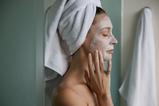 Young woman in bathroom wrapped in towels with facial mask. Home spa and skin care concept.