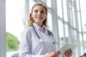 healthcare, technology and medicine concept - smiling female doctor with stethoscope taking notes at tablet pc computer.