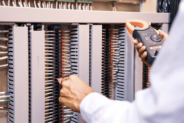 Electrical engineer using digital multi-meter measuring equipment to checking electric current voltage at circuit breaker in main power distribution board.