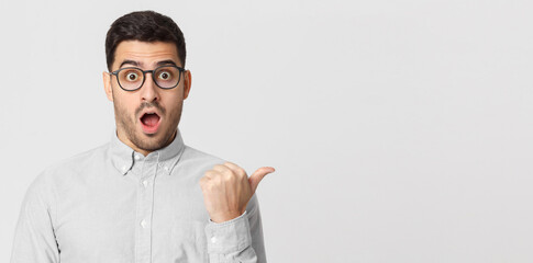 Naklejka premium Banner of surprised young man in shirt pointing with thumb to the right, isolated on gray background with copy space