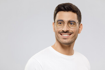 Young handsome man wearing white t-shirt and glasses looking aside with confident smile as if making future plans, isolated on gray background