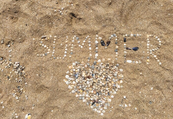A large heart of seashells laid out on sea sand with the inscription and letters summer. Photography, concept, top view.