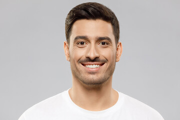 Fototapeta premium Headshot portrait of young smiling handsome man wearing white t-shirt, isolated on studio gray background
