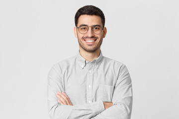 Smiling handsome man in shirt and round glasses standing with crossed arms isolated on gray