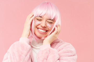 Young happy girl in fur coat with pink hair, touching her head and dancing to music with closed...