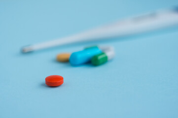 Red pill on a blue background and other medicines and a thermometer in the background