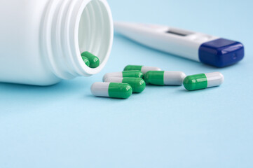 pack of medicine with green capsules lies on a blue background next to a thermometer.