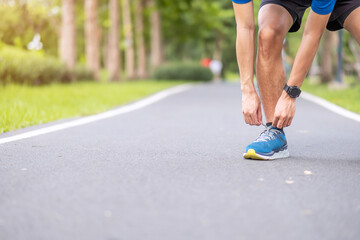 Young adult male in sportswear tying shoelace in the park outdoor, athlete runner man ready for running and jogging in morning. Exercise, wellness, healthy lifestyle and workout concept