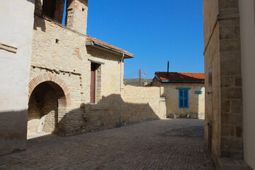 A paved street of a Cypriot village with stone houses with blue Windows against a blue sky. Cyprus.
