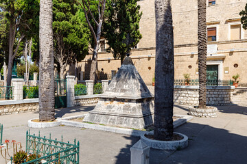 The monument with a metal cross in front of the facade of the Stella Maris Monastery which is...