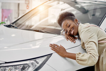 smiling black lady hugs her new auto in cars showroom. young woman fulfill her dream, lies on car - obrazy, fototapety, plakaty