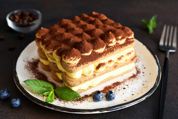 Italian traditional tiramisu dessert in a plate on a concrete background.
