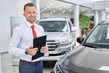 confident caucasian smiling car dealer at work, man in white formal shirt ready to talk about cars,...
